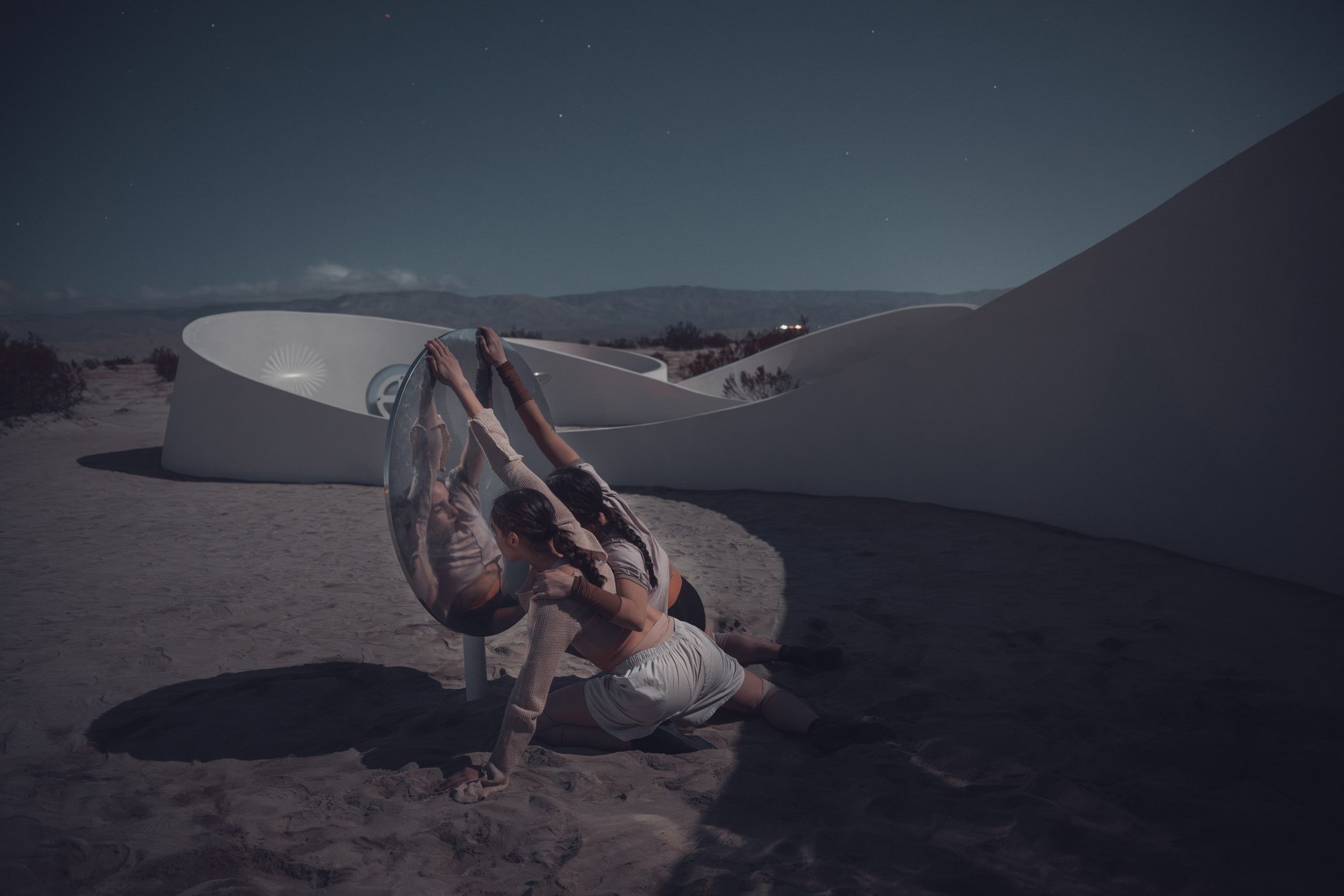 Dancers gathered beside a curved concrete ribbon under moonlight