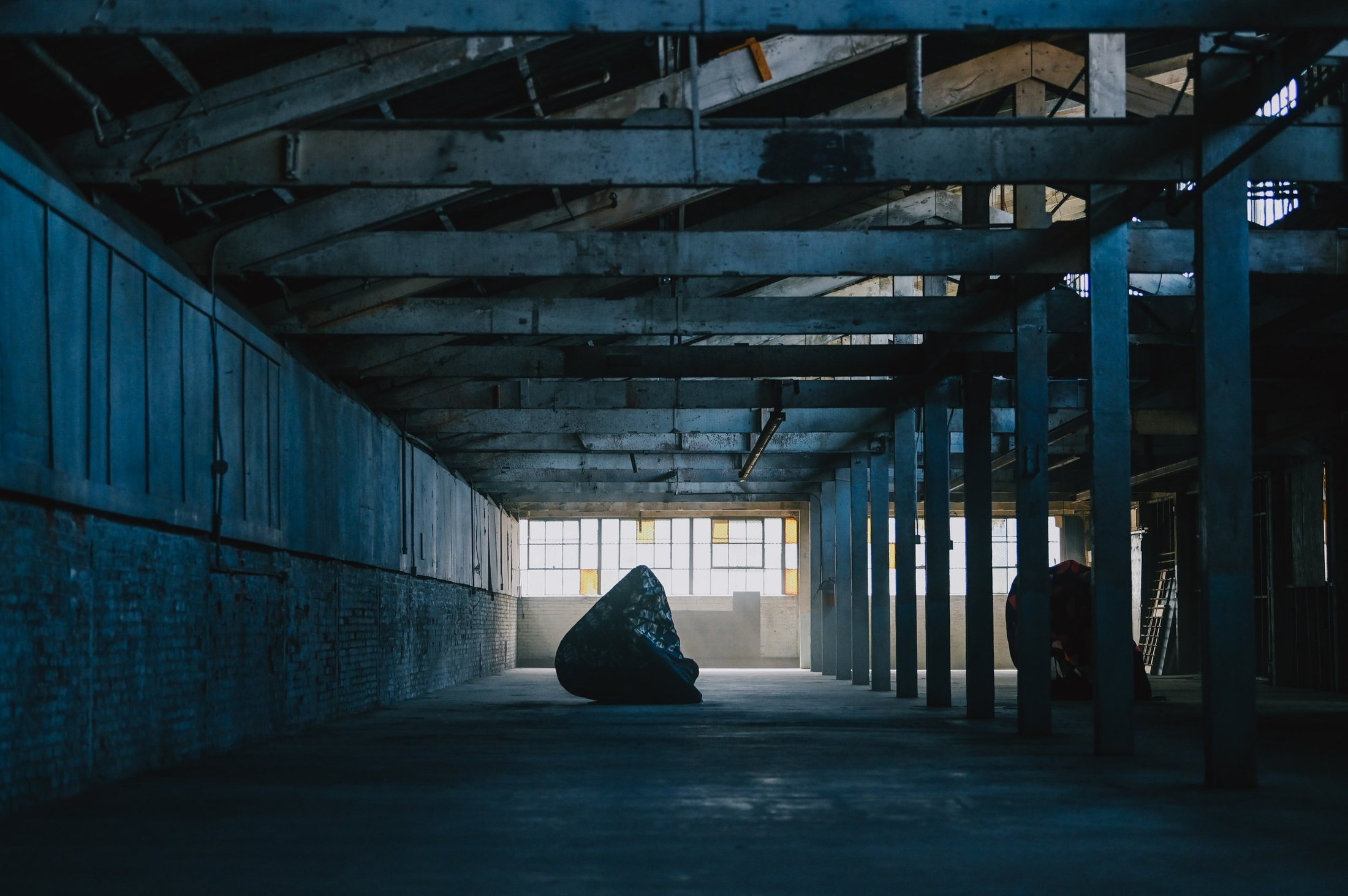 A fabric-covered figure inside a long concrete warehouse